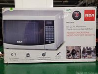 Photograph of the RCA microwave oven box showing product image and specifications including 0.7 cu ft capacity, child lock, electronic touchpad, and 700 watts power.