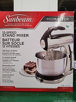 Front view of the boxed Sunbeam MixMaster 12-speed stand mixer, showing product details and features on the packaging.