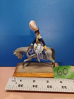 Side view of the painted British cavalryman mounted on a horse figurine on a wooden base with a ruler measuring size.