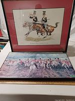 Two framed British military prints displayed with a wooden ruler for scale. Black frames, maroon mat on the mounted 17th Lancers print.
