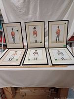Six vintage British military uniform prints, each framed and arranged three upright and three laid flat on a white fabric surface with a measuring ruler along the bottom for scale.