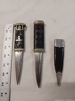Two sgian dubh knives and sheath arranged next to a ruler showing length