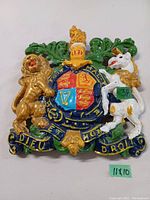 Front view of cast metal painted UK coat of arms, showing detailed lion, unicorn, shield, and crown with motto.