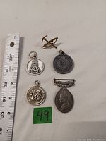 Five metal military badges and medals laid on white background with ruler for scale