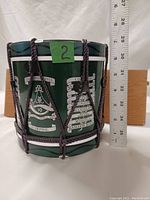 Front view of green drum style plastic ice bucket displaying 10th Gurkhas badge and multiple battle honors with measuring ruler beside showing about 8 inches height.