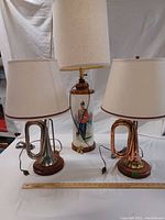 Front view of the set of three lamps showing two bugle instrument lamps and one painted ceramic military soldier lamp