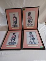 Four framed vintage British military prints, arranged in a square, showing four soldiers in traditional Scottish regimental uniform. Each has a pink matte and thin black frame. Some fading visible on matte.