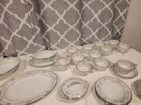 Array of teacups with saucers, gravy boat, creamer and covered sugar bowl alongside small plates on table.
