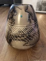 Raku pottery vase with black crackle smoke pattern and geometric engravings, turquoise detail on front.