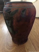 Front side view photo of the unique rounded pottery vessel with dark coppery glaze and patterns.