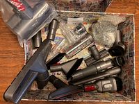 Box containing Dyson vacuum accessories arranged showing various brush heads, extension tubes, and one motorized head still in packaging.