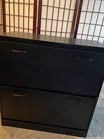 Front view of black IKEA shoe cabinet with two compartments closed, showing metal handles for opening.