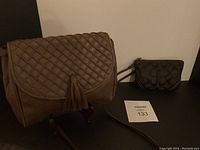 Photo showing the brown vintage Borelli P. Italian leather purse with a quilted flap, tassel detail, and long strap, positioned next to a small black embossed fabric wristlet with large C monogram pattern.