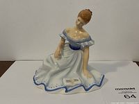 Front view of Royal Doulton figurine showing lady kneeling and reading a book with white and blue dress.
