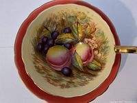 Top-down view of cup interior showing peaches, grapes, leaves and gold handle