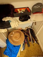 Photo showing various hats, belts, gloves, umbrellas, poncho, garment bags, shoe molds/stretchers and handkerchief arranged on floor and shelf