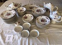Full set of floral china laid out on a beige tablecloth including teapot, soup pot, plates, bowls, and cups.