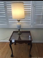 Wood end table with glass top and clawfoot legs, showing full table and lamp on top