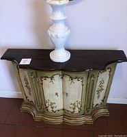 Front view of the ornately decorated wood entry table with floral details and metal accents, showing the top surface and front panel designs.