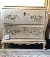 Front view of one dresser showing two drawers with decorative metal hardware and bombe silhouette