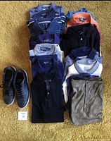 Multiple folded men's polo shirts in various colors and patterns with a pair of black Adidas tennis shoes size 10.5 on carpeted floor.