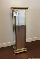 Front view of tall rectangular mirrored pedestal stand with metal trim and tarnish