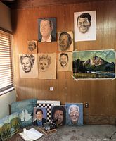Wall display showing multiple celebrity and presidential portraits in charcoal and paint, landscape paintings on canvas, and a wooden checkerboard on floor.