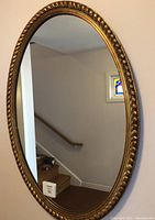 Full view of the oval mirror leaning against a wall, showing reflections and overall size.