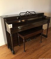 Full view of the Andrew Koehler upright piano with matching bench placed on a wooden floor against a plain wall