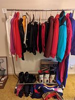 View of ski clothing hanging on metal rack with ski boots and folded gloves and socks underneath