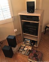 Stereo sound system in beige cabinet with glass door, showing Panasonic stereo components, Philips CD changer, two Panasonic speakers, and media including tapes, records, CDs on floor.