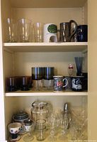 Shelf with clear glasses, decorated mugs, and shot glasses