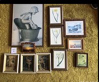 Overview of all framed art laid out on yellow carpet, showing variety of themes including bath sculpture, botanical flowers, coastal scenes, and dancers