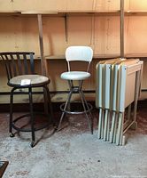 Photo showing the white microfiber swivel stool, the black metal stool, the set of four white TV trays with gold trim, and the matching foldable stand.