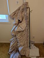 Two ruffled upholstered fabric valences hanging from a black metal stand, showing texture and pattern details.