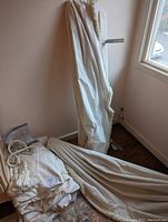 Photo showing folded curtains with decorative trim placed by a window near the floor.