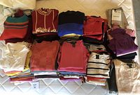 Overview of folded sweaters, tops, camisoles and sock packs arranged on mattress