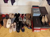 Overall lot of women's shoes and slippers arranged on carpet and stacked shoe boxes.