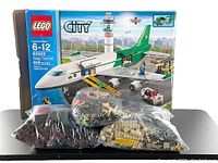 Box front of LEGO City Cargo Terminal set with visible 658 piece count, age 6-12, beside bags of loose LEGO bricks and parts.