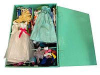 Photo showing open teal wooden box with various Barbie and handmade doll dresses and clothing inside.