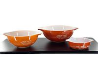 Set of three Pyrex Autumn Harvest pieces including two nesting mixing bowls and one casserole dish arranged in a row.