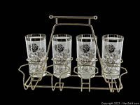 Set of four vintage highball glasses with rose pattern and silver rims sitting in a silver metal holder designed for eight glasses, shown on black background