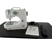 Full view of Singer Quik Fix mending sewing machine with power cord, foot pedal, and instruction manual displayed on black table.