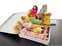 Nine vintage Barbie dolls mainly in 1960s-1970s fashion outfits in a white case showing arrangement and condition of dolls.