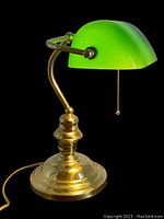 Side view of vintage banker desk lamp showing green glass shade, brass stand, and base with patina and wear