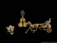 Photo showing the brass door knocker, brass bell stamped 'England', and brass horse and driver figurine missing reins against black background.