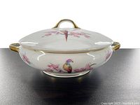 Photo of the covered dish from the side showing the Bird of Paradise and floral designs on the body and lid, gold-trimmed handles and lid handle.