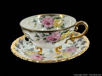 Photo showing the vintage hand-painted floral Shafford teacup on its gold gilded feet alongside the matching reticulated saucer with pink and yellow roses and gold trim.