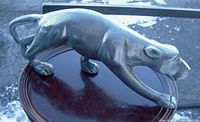 Side angle of large silvered metal cougar or jaguar statue with stylized muscle details and curled tail.