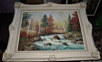 Framed oil painting on board signed by Anna Jalava showing a river with rapids and mixed forest in autumn colors, in a large white ornate frame.